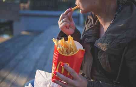 jemand hält eine rote Tüte Pommes in der Hand und steckt sich gerade eine Pommes Frites in den Mund