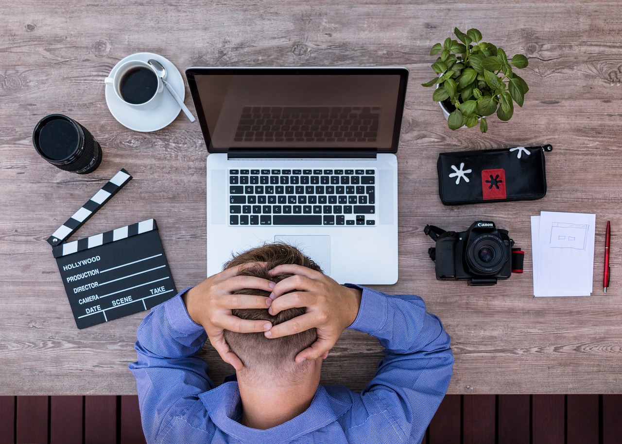 Man sitzt mit Hände hinterm Kopf über Labtop. Verzweifelt, von oben fotografiert. Hier Burnout