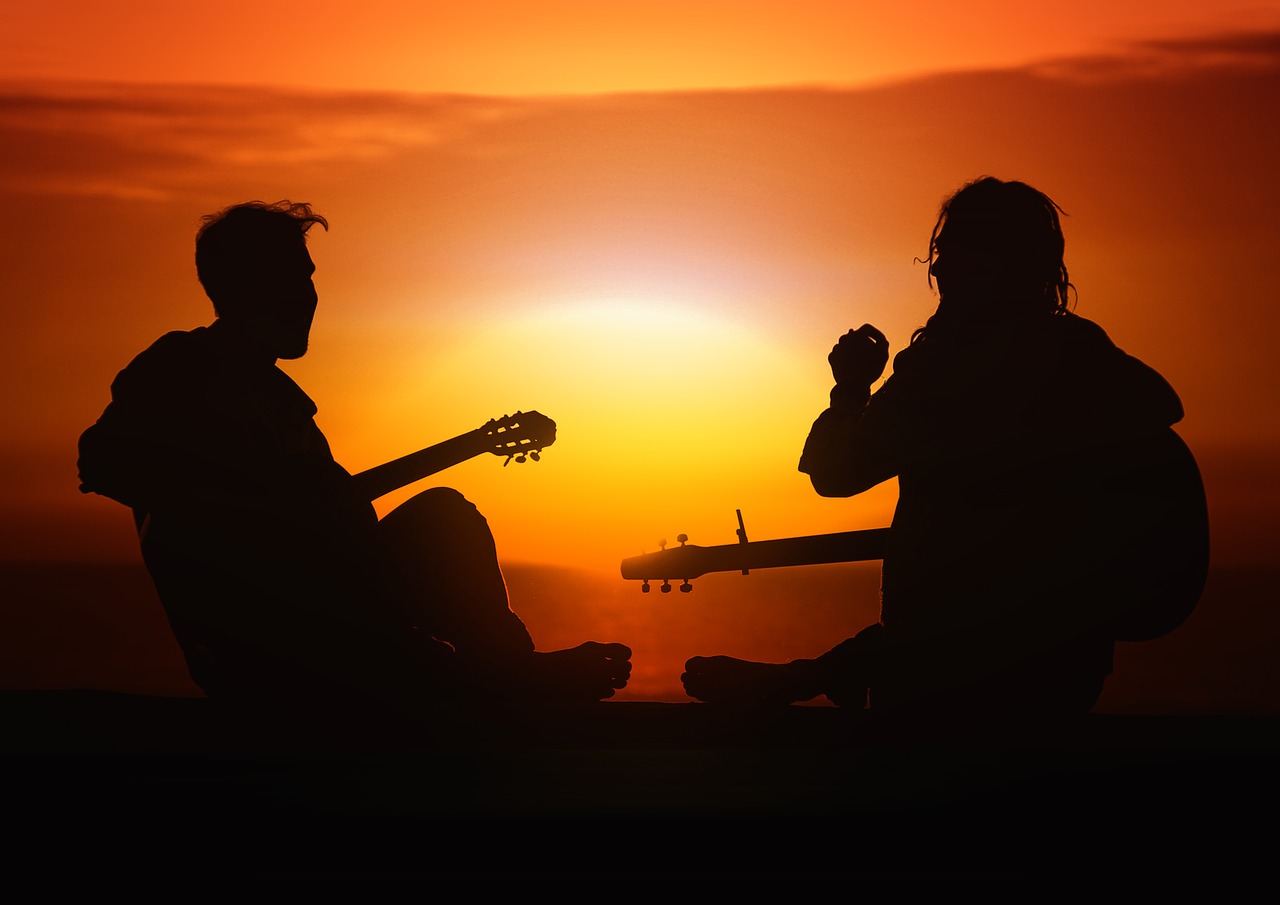 2 Personen mit Gitarre vor rotem Sonnenuntergang. Nur die Silhouette ist erkennbar. Hier: Burnout