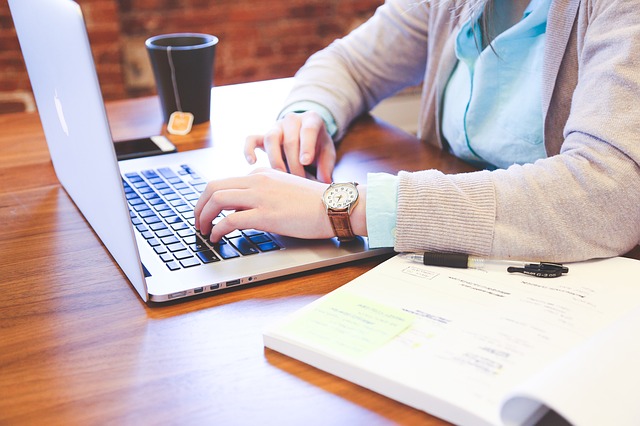 Frau sitzt am Labtop mit Tasse Tee und Buch und schriebt, hier: Geld verdienen mit Texten und Bildern, Geschäftsidee finden