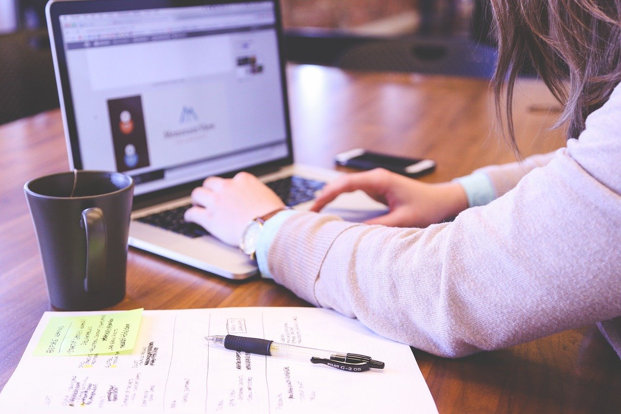 Eine Person sitzt am Laptop mit einer Tasse Kaffee und arbeitet