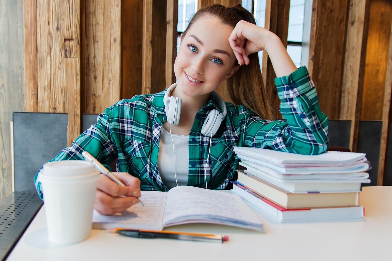 Eine junge Studentin am Schreibtisch, den Kopf aufgesetzt und freundlich lachend.