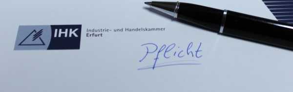 IHK Briefpapier mit dem Logo der IHK Erfurt, darauf ein Kugelschreiber und das handschriftliche Wort "Pflicht"