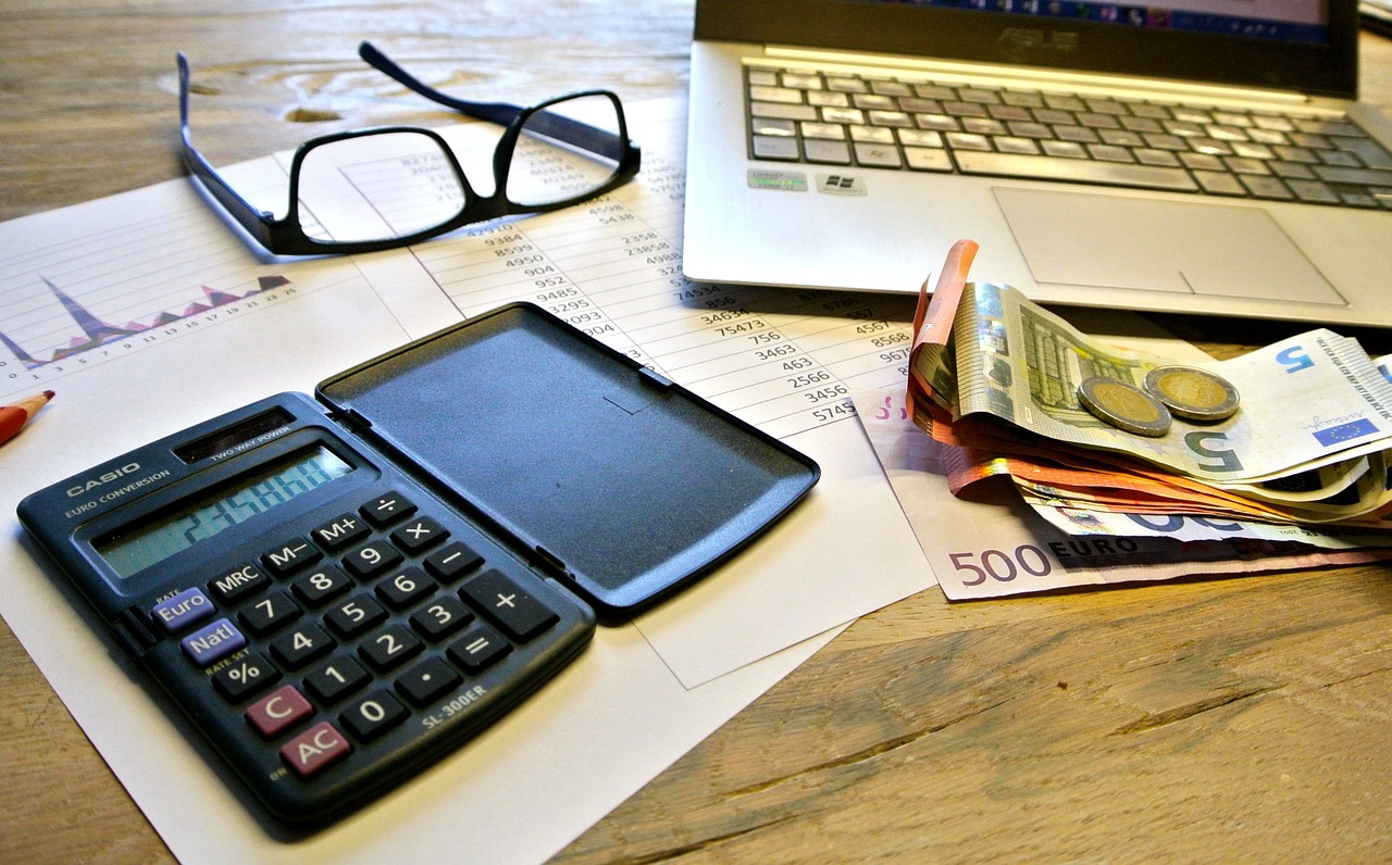 Laptop, Brille, Taschenrechner, Geld auf einem Holztisch