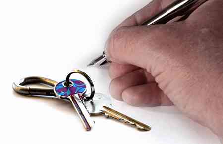 Schlüssel zu den Geschäftsräumen auf dem Tisch, Hand mit Stift zur Unterschrift