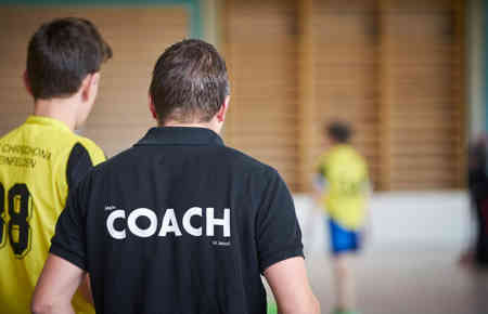 Trainer mit Rücken zum Betrachter gewandt. Auf seinem T-Shirt steht Coach, hier Life Coach werden