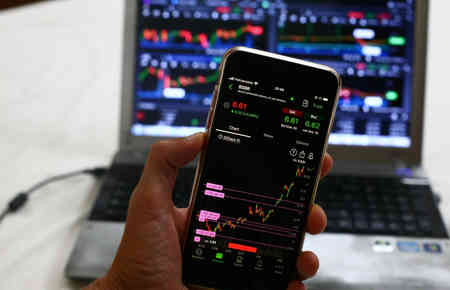 mobil telefon mit aktien chart vor einem Notebook mit aktien und Brsenansicht, hier: Mit aktien apps geld verdienen