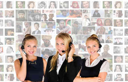 Drei Frauen mit Headset im Kundenservice vor einer Bilderwand mit vielen Personen, was sicherlich die Kunden darstellen soll.