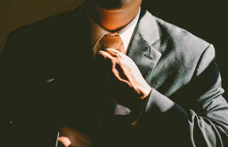Ein Mann fasst mit seiner Hand an den fertiggebundenen Schlips, hier: korrekte Messebekleidung
